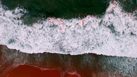 Aerial-view-of-a-wave-breaking-on-a-golden-sandy-beach,-The-mesmerizing-patterns-of-foam-and-surf