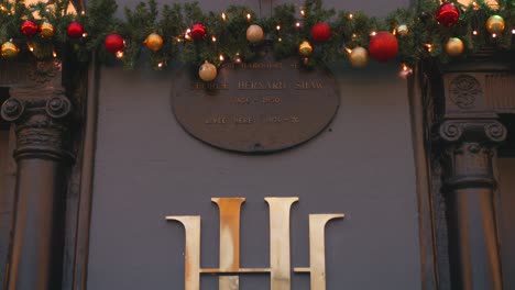 Tilt-down-shot-of-sign-logo-in-front-of-Harcourt-Hotel-with-colorful-Christmas-decorations-in-Dublin,-Ireland