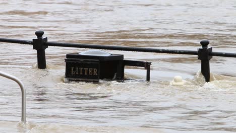 Fast-flowing-flood-water-covering-railings-and-litter-bin-at-Bewdley,-Worcestershire