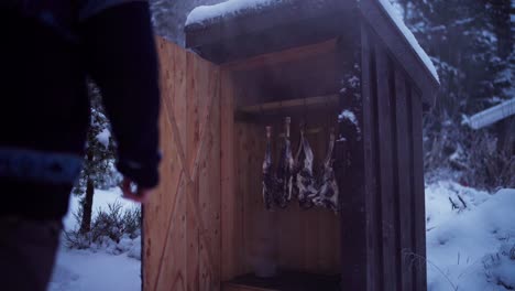 Man-Checks-On-Deer-Meat-Smoking-Inside-Smokehouse-Shed-In-Norway-During-Winter