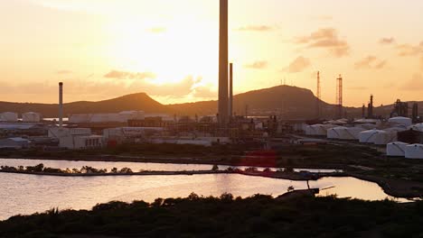 Große-Erdöltanks-Mit-Treibstoff-Und-Fackelstapeln,-Die-Bei-Sonnenuntergang-In-Curaçao-Von-Hinten-Beleuchtet-Werden