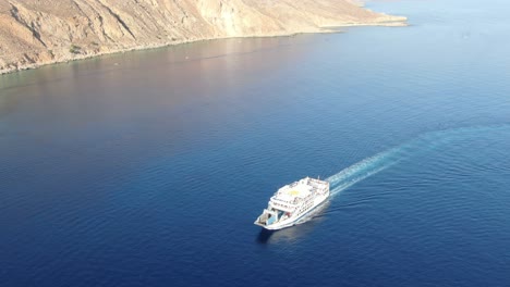 Drone-view-in-Greece-flying-over-a-ship-on-the-blue-mediterranean-sea-next-to-a-brown-hill-on-a-sunny-day