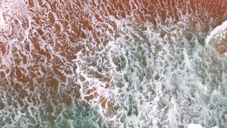 Luftaufnahme-Einer-Welle,-Die-An-Einem-Goldenen-Sandstrand-Bricht,-Die-Faszinierenden-Muster-Aus-Schaum-Und-Brandung