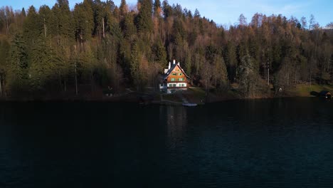 Aerial-push-in-to-cabin-lake-house-with-shimmering-reflection-in-dark-blue-water