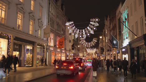 Shot-of-cars-and-pedestrians-moving-along-illuminated-street-with-Christmas-decorations-at-night-time