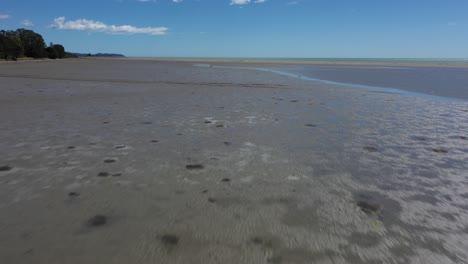 Drone-flyover-mudflats-towards-sandbar-on-sunny-day-with-blue-sky