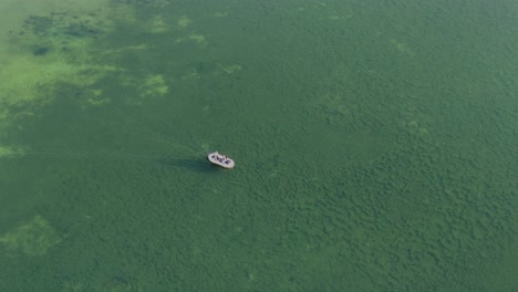 Ein-Schlauchboot-Segelt-Langsam-über-Einen-Flachen-See,-Wobei-Der-Pflanzenboden-Von-Einer-Drohne-Aus-Sichtbar-Ist