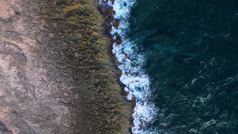 Drone-top-down-pan-across-jagged-rocky-shoreline-with-volcanic-basalt-and-sharp-edges-in-water