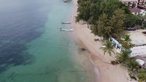 Descending-drone-shot-of-a-beach-in-Koh-Tao-Thailand-with-palm-trees-and-small-waves-on-the-sand