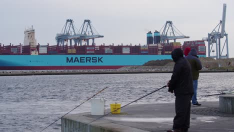 Fischer-Angeln-Mit-Maersk-Frachtschiff,-Das-Im-Hintergrund-Beladen-Wird