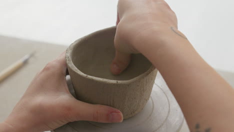 Skillfully-molding-a-clay-cup's-surface-with-fingers,-creating-intricate-texture-in-a-charming-studio