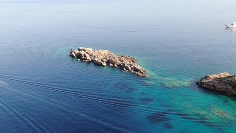 Drone-view-in-Greece-flying-over-blue-sea-in-Loutro-with-rocks-on-the-water-on-a-sunny-day