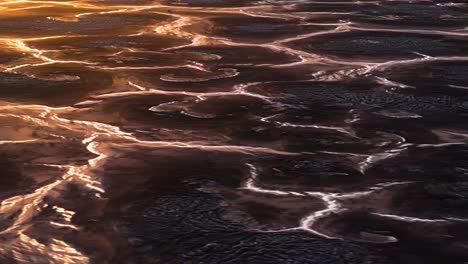 Aerial-parallax-around-braided-streams-of-water-between-large-mounds,-natural-earth-wasteland-textured-pattern