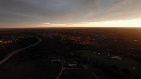 Aerial-shot-of-a-sunset-at-golden-hour-over-suburban-landscape,-forward-dolly