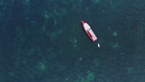 Top-down-drone-shot-of-a-red-boat-in-Thailand-with-coral-under-the-water