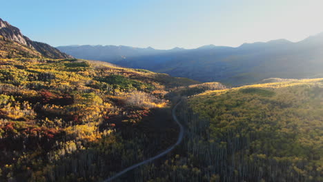 Stunning-bright-bluebird-sun-flare-morning-autumn-Aspen-tree-forest-fall-golden-yellow-colors-Kebler-Pass-aerial-cinematic-drone-Crested-Butte-Gunnison-Colorado-Rocky-Mountains-backward-reveal