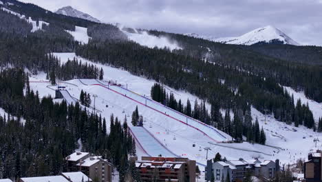 Snow-making-Half-Pipe-Big-Air-Jump-ski-snowboard-gondola-ski-lift-aerial-drone-cinematic-Copper-Mountain-Colorado-Winter-December-Christmas-Ski-runs-trails-landscape-cloudy-Rocky-Mountains-backwards