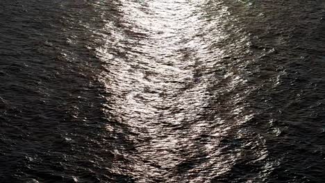 Drone-push-in-as-light-glistens-on-leathery-textured-wave-ripples-on-ocean-water-surface