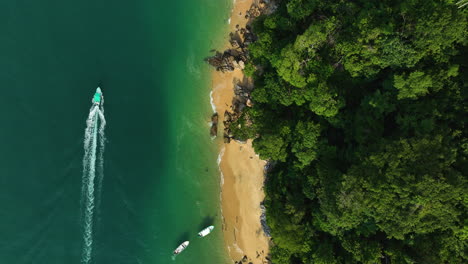 Top-down-drone-shot-above-a-boat-driving-along-the-coast-of-tropical-jungle