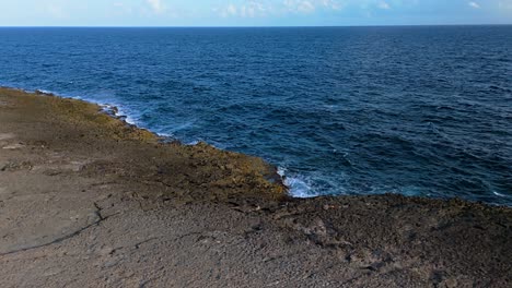 Drone-trucking-pan-across-eroded-basalt-volcanic-rocky-landscape-on-coast-of-deep-blue-ocean-water