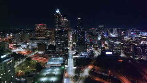 Toma-Cinematográfica-De-Un-Drone-Del-Horizonte-De-Rascacielos-Iluminados-De-La-Ciudad-De-Atlanta-En-Georgia-Por-La-Noche:-Tráfico-En-La-Intersección-Debajo-De-Los-Puentes