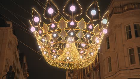 Tilt-down-shot-of-hanging-Christmas-decoration-light-over-the-street-of-London,-UK-at-night-time-in-the-shape-of-a-crown