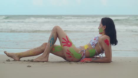 Vibrant-body-paint-adorned-the-bikini-clad-figure-of-a-young-girl,-creating-a-striking-scene-on-a-Tropical-beach-in-the-Caribbean-with-ocean-waves-in-the-background