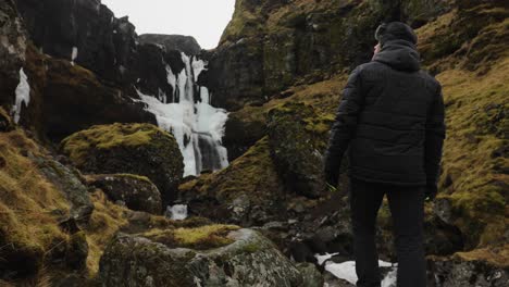 Tourist-stand-in-dark-Icelandic-mountain-environment-with-moss-near-waterfall