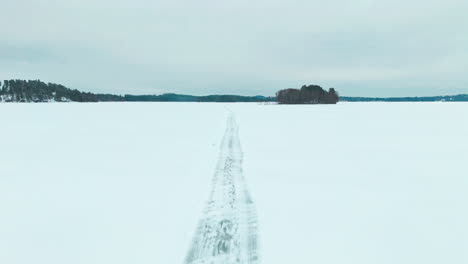 Flying-along-a-road-on-frozen-lake-ice-to-reveal-a-snowy-forest-in-the-horizon
