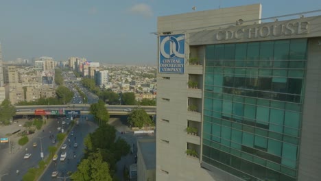 Drone-shot-of-CDC-Building-beside-a-busy-street-during-daytime-in-Karachi,-Pakistan