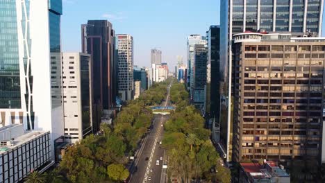 Aerial-flight-over-main-road-in-mexico-City-between-skyline-and-Angel-of-Independence-monument-roundabout-at-sunrise