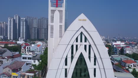 Strange-modern-church-building-and-cityscape-panorama-on-a-sunny-day-crane-shot-revealing-red-cross-and-high-rise-buildings