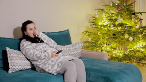 Eine-Frau-Sitzt-Vor-Dem-Fernseher-Und-Sitzt-Auf-Einer-Couch-Neben-Einem-Leuchtenden-Weihnachtsbaum