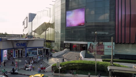 Käufer-Gehen-In-Ein-Einkaufszentrum-Hinein-Und-Wieder-Heraus,-Während-Einige-Vorbeikommen-Und-Streetfood-Von-Händlern-Kaufen,-Die-Vor-Einem-Einkaufszentrum-In-Bangkok,-Thailand,-Verkaufen