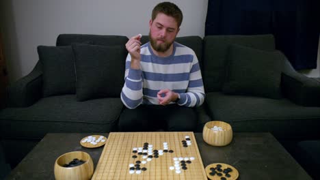 Bearded-man-thoughtfully-holds-Go-stone,-plots-strategic-move,-then-confidently-plays-piece-and-crosses-his-arms-with-smug-smile,-proud-of-his-skillful-play