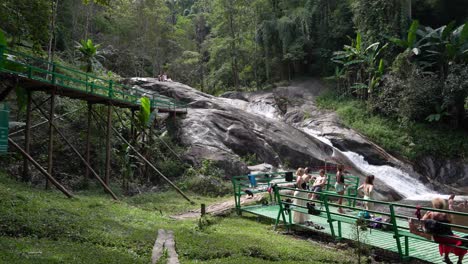 Group-of-tourists-waiting-on-green-metal-platform-waiting-to-go-down-waterfall---Mo-Pang,-Thailand