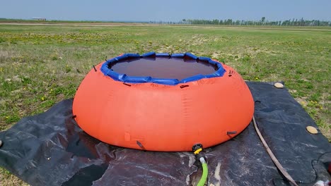 An-orange-water-tank-on-airport-property,-connected-to-a-pump,-amidst-a-grassy-field-under-a-clear-sky