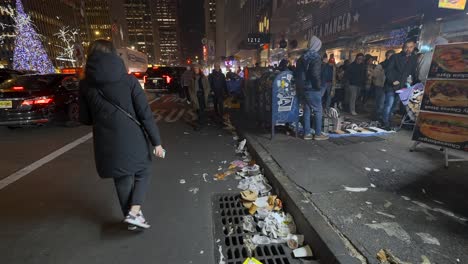 People-walking-along-trash-filled-street,-at-night,-in-New-York-City