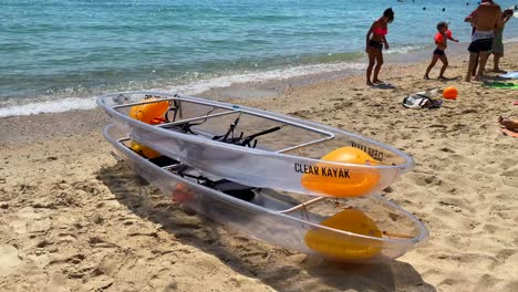 Two-transparent-clear-kayaks-at-a-beautiful-beach-in-Cavalière-Lavandou-on-a-sunny-summer-day-in-South-of-France,-fun-water-sport-holiday-vacation-activity-in-the-sea,-4K-shot