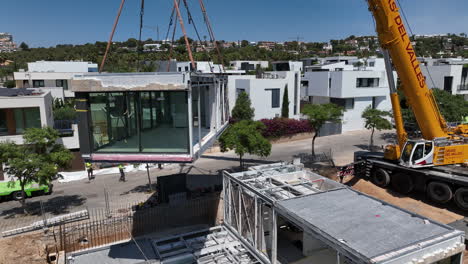 Crane-lifting-whole-room-with-windows-of-modular-home,-aerial-view