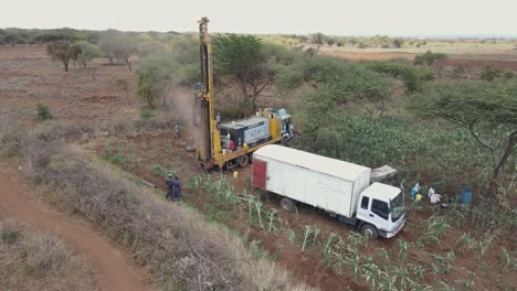 Engineers-supervise-drilling-borehole-well-on-African-farmland,-aerial