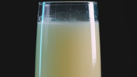 Yellow-sparkling-soft-drink-in-glass-against-black-background,-close-up-pan