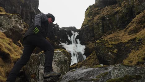 Man-climb-volcanic-rock-to-reach-sightseeing-area-near-Icelandic-waterfall