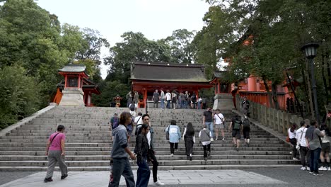 Many-tourists-climbing-the-stairs-of-the-Fushimi-Inari-Shrine,-visiting-the-paths-of-the-ancient-temple-in-Japan,-learning-about-its-architecture,-culture,-history-and-mountains