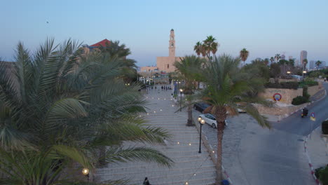 Jaffa-Old-city-at-sunset-with-lots-of-families-visiting-restaurants,-shops-and-bars-in-the-port---push-in-drone-shot-between-the-date-trees