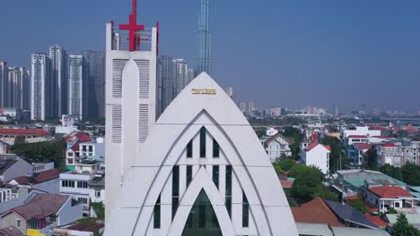 Strange-modern-church-building-and-cityscape-panorama-on-a-sunny-day-crane-shot-revealing-red-cross-and-high-rise-buildings