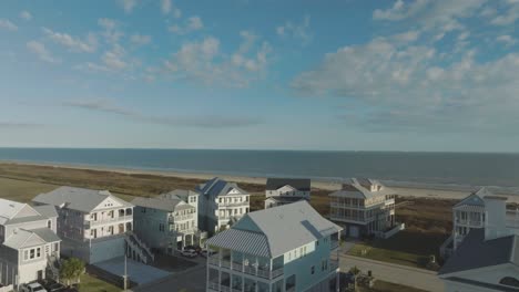 An-aerial-view-of-beach-houses-overlooks-Galveston-Beach,-set-against-a-backdrop-of-blue-skies-and-white-clouds-on-East-Beach-in-Galveston-Island,-Texas