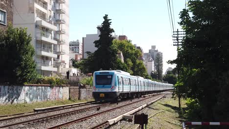 Train-Departs-in-Slow-Motion-Park-Railway-in-Green-Landscape-and-Home-Buildings-in-Sarmiento-Line