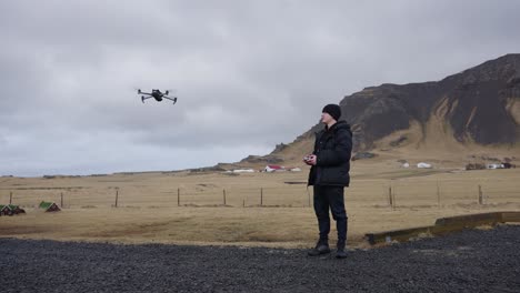 Drone-pilot-on-black-gravel-road-use-remote-control-to-fly-toward-mountain