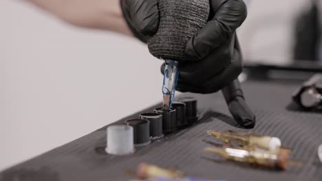 Tattoo-Artist-Dips-The-Tip-Of-The-Needle-Cartridge-Into-A-Filled-Ink-Cap-On-The-Table